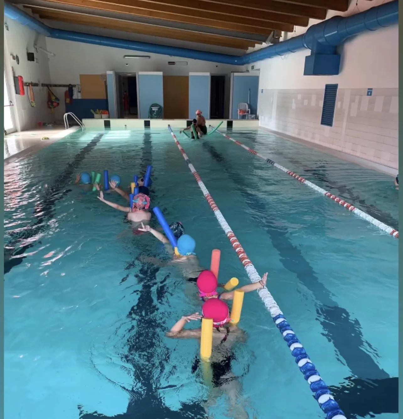 Bambini in fila in acqua con tubi galleggianti durante una lezione di nuoto